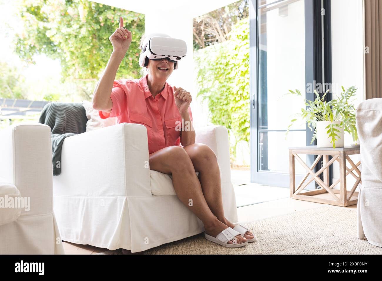 Senior caucasian woman using virtual reality headset, sitting on white armchair Stock Photo