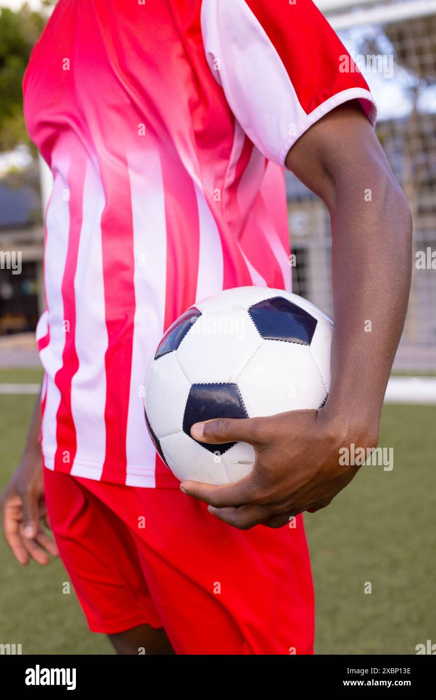 African American soccer player holds soccer ball, wears red and white