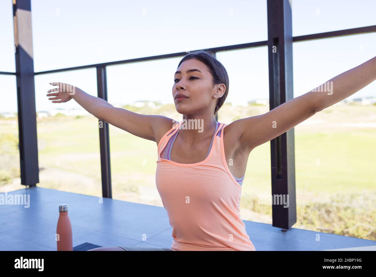 Happy biracial woman doing yoga with arms wide open, looking relaxed and focused Stock Photo