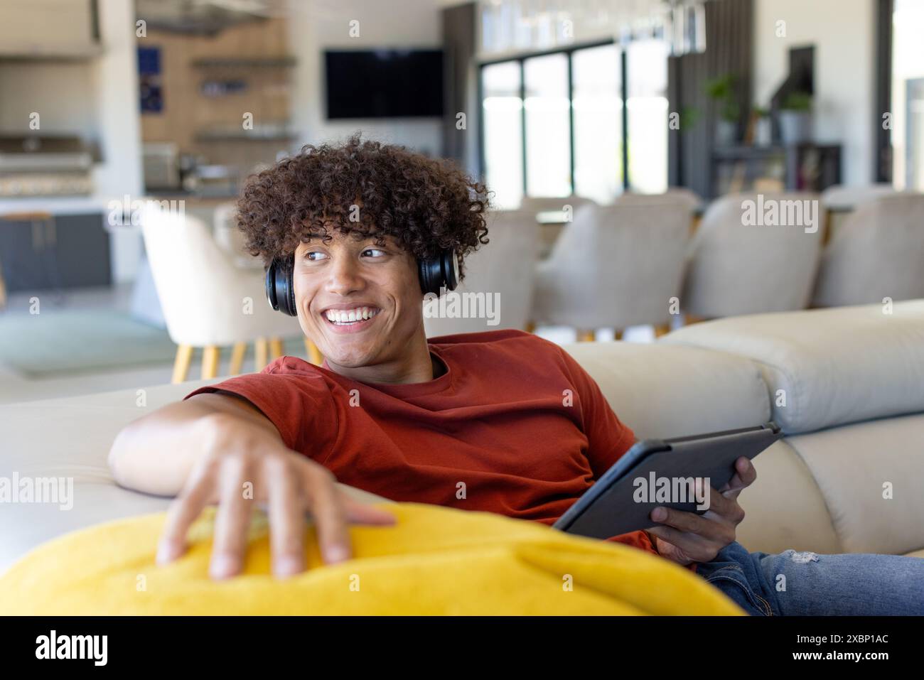 Happy biracial man relaxing with headphones, tablet in hand, smiling on a couch Stock Photo