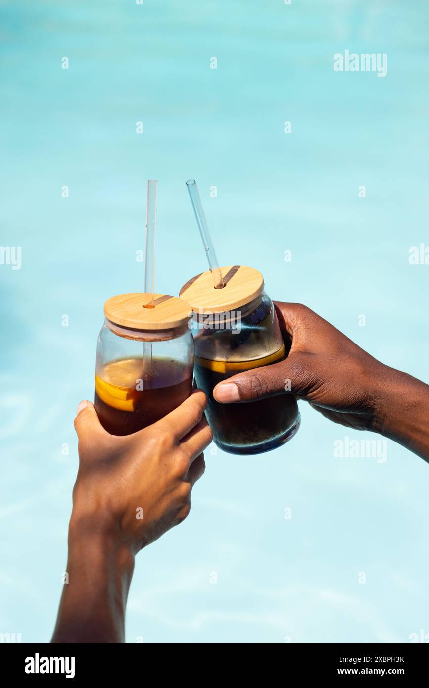 A diverse couple enjoys drinks by the pool under summer sun on a joyful vacation Stock Photo