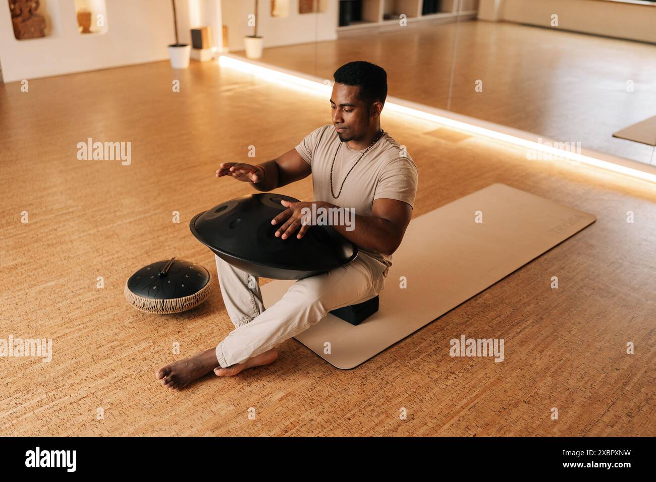 High-angle shot of African man in trance enjoying playing by hands on glucophone sitting cross-legged on floor at home. Silence calm filling room by Stock Photo
