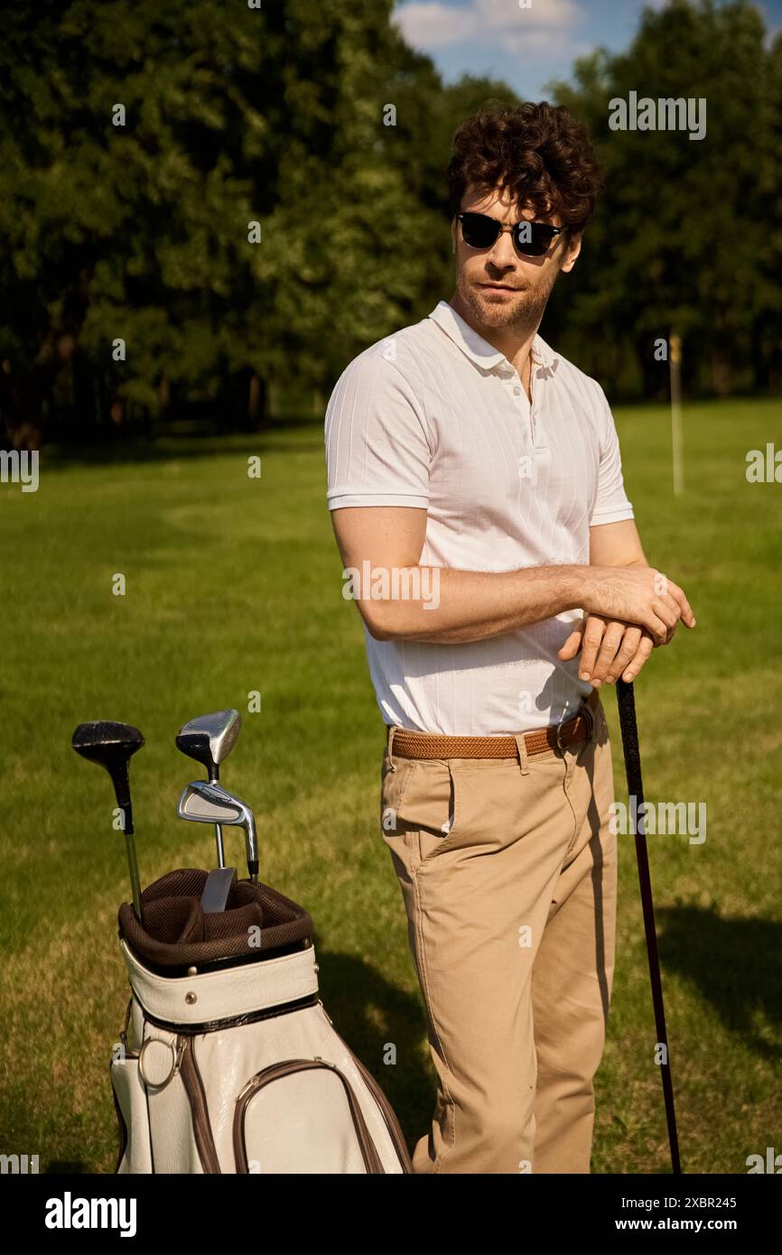 A man stands elegantly next to his golf bag on a green field at the golf club, embodying an old money style lifestyle. Stock Photo