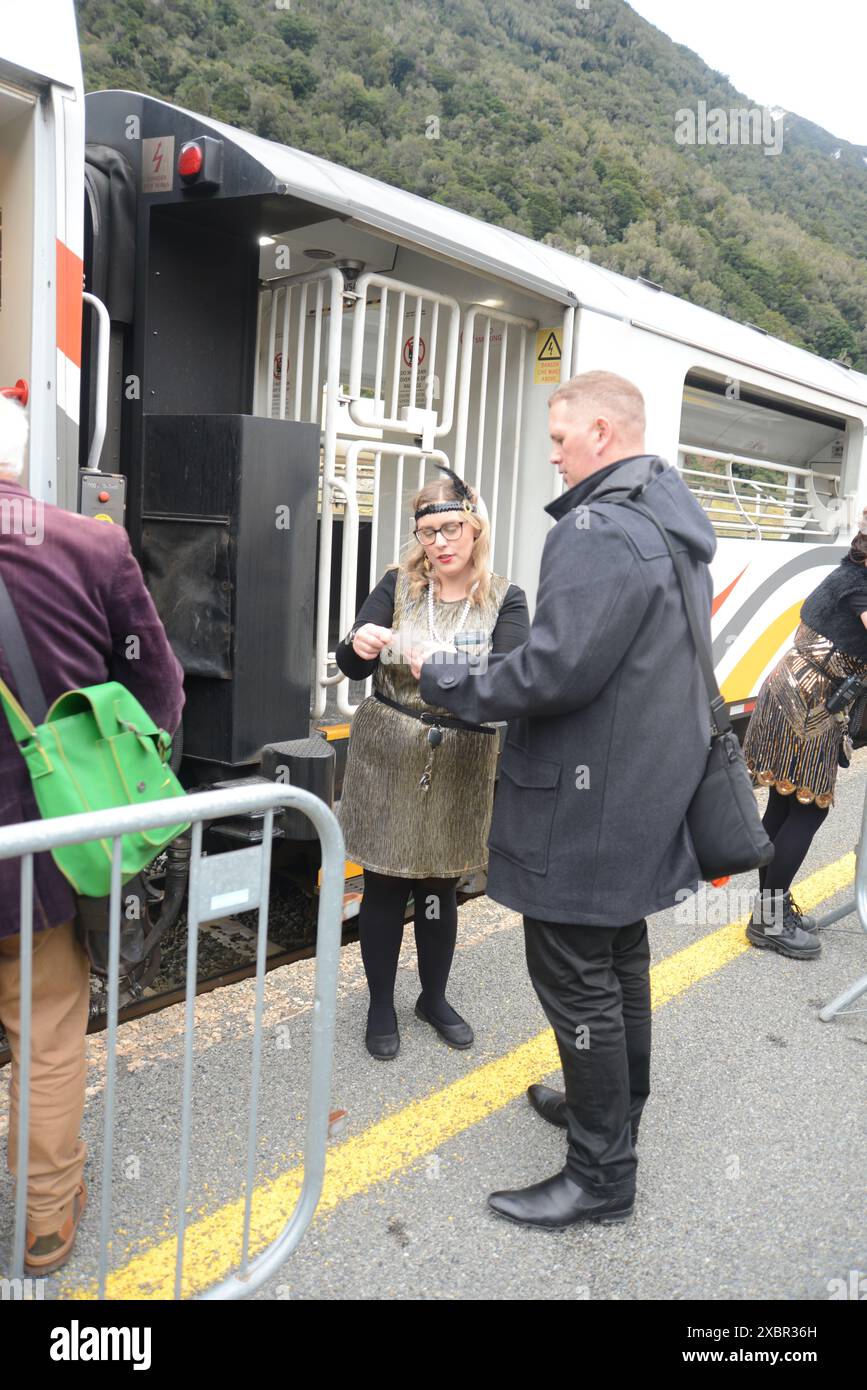 OTIRA, NEW ZEALAND, AUGUST 4, 2023:A female staff member of KiwiRail dressed in 1920's costume directs a passenger on the TranzAlpine journey to celebrate the 100th anniversary of the opening of the Otira Tunnel, New Zealand Stock Photo