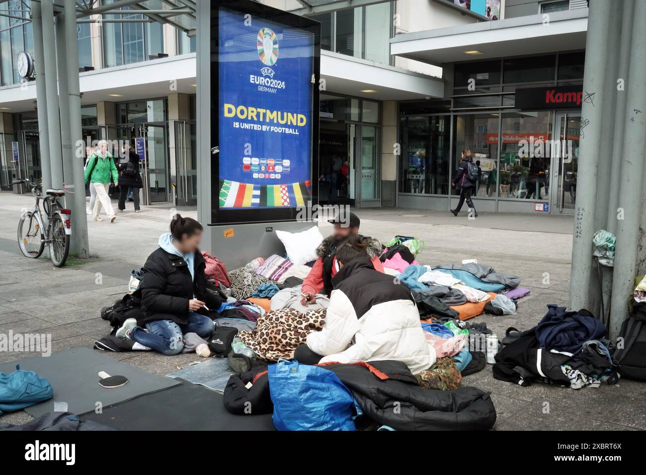 Homeless people camp in front of a poster for the EURO2024 European