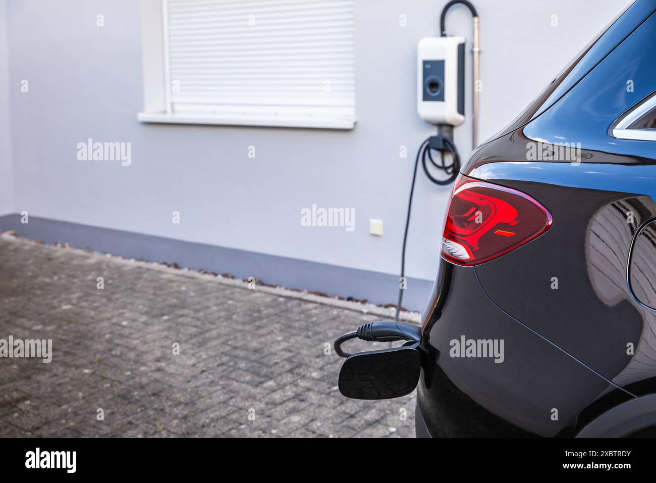 Generic electric vehicle EV hybrid car is being charged from a wallbox on a contemporary modern residential building house Stock Photo