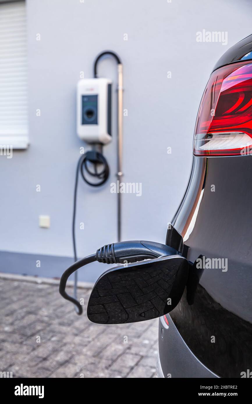 Generic electric vehicle EV hybrid car is being charged from a wallbox on a contemporary modern residential building house Stock Photo