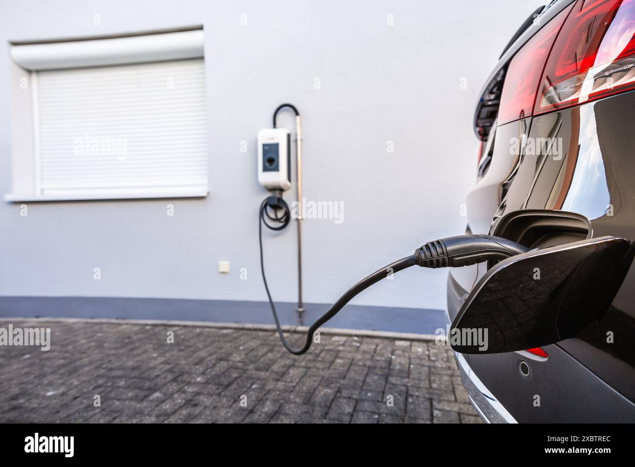 Generic electric vehicle EV hybrid car is being charged from a wallbox on a contemporary modern residential building house Stock Photo