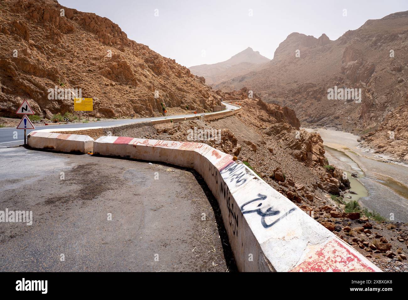 Rocky Rpad Sign A winding mountain road with a concrete barrier and caution signs in a ...