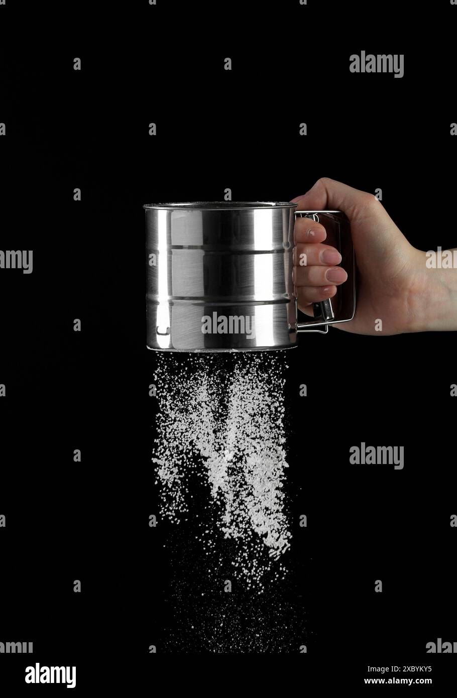 Woman sieving flour against black background, closeup. Space for text ...