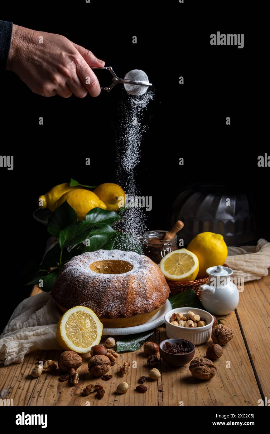 Woman's hand pouring sugar falling on bundt on table Stock Photo