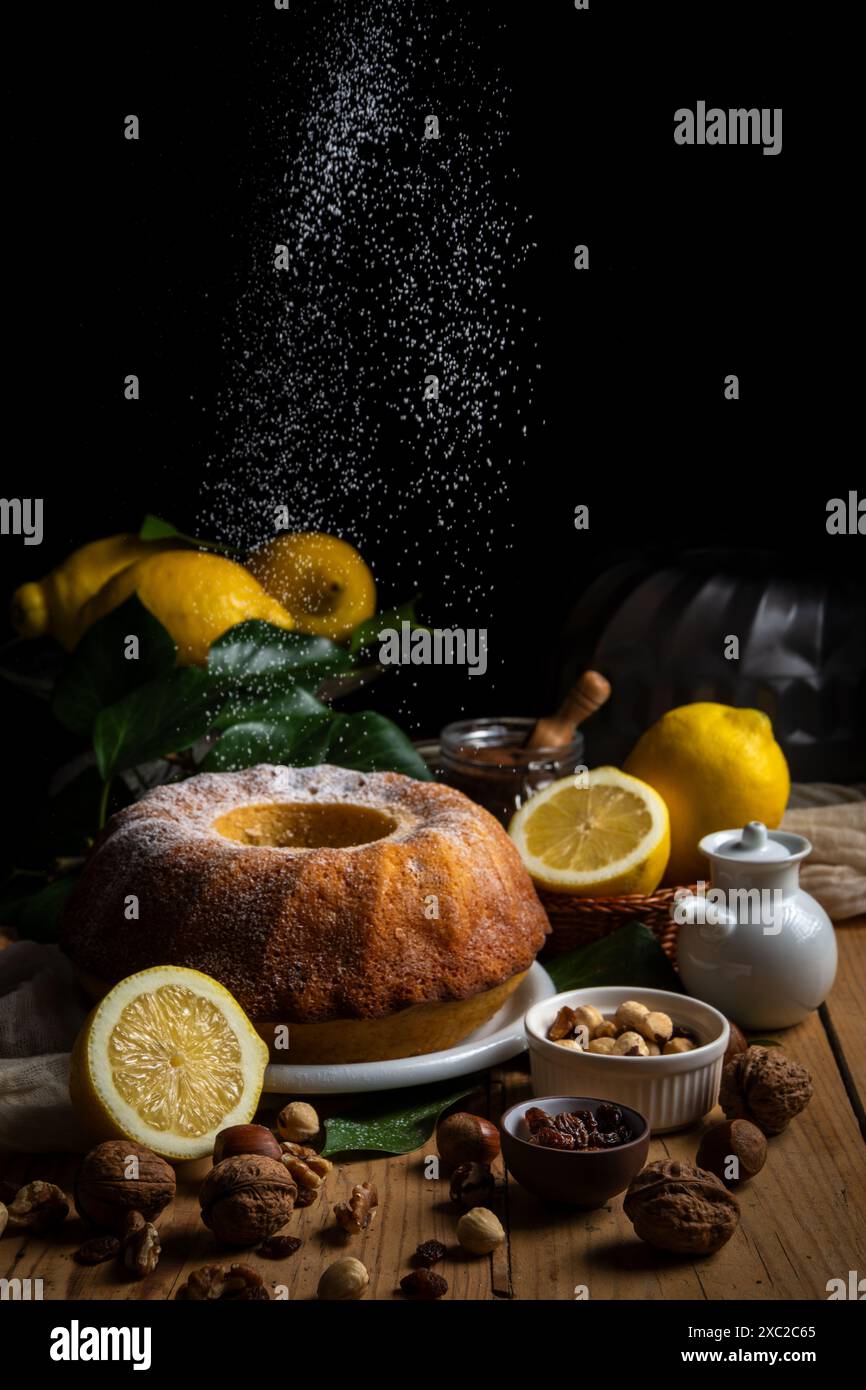 Sugar falling on bundt on table with lemons Stock Photo