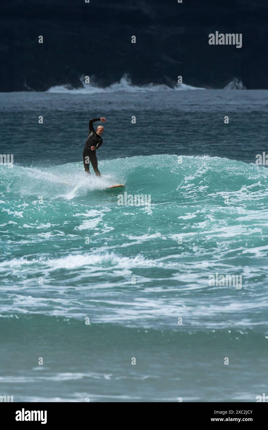 A surfer riding a wave at the iconic Fistral Beach in Newquay in ...