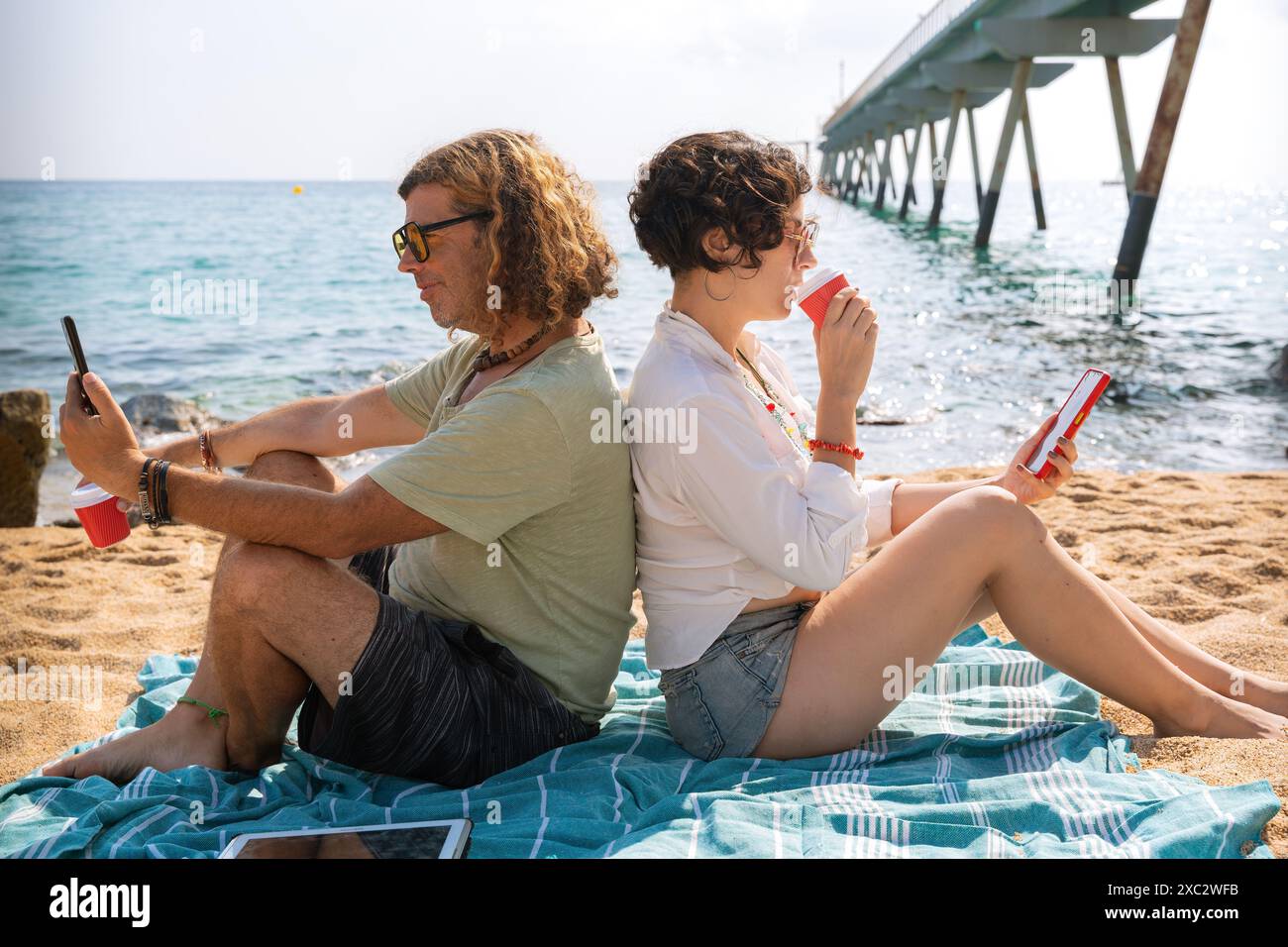 couple on the beach browsing smartphones apps. Stock Photo
