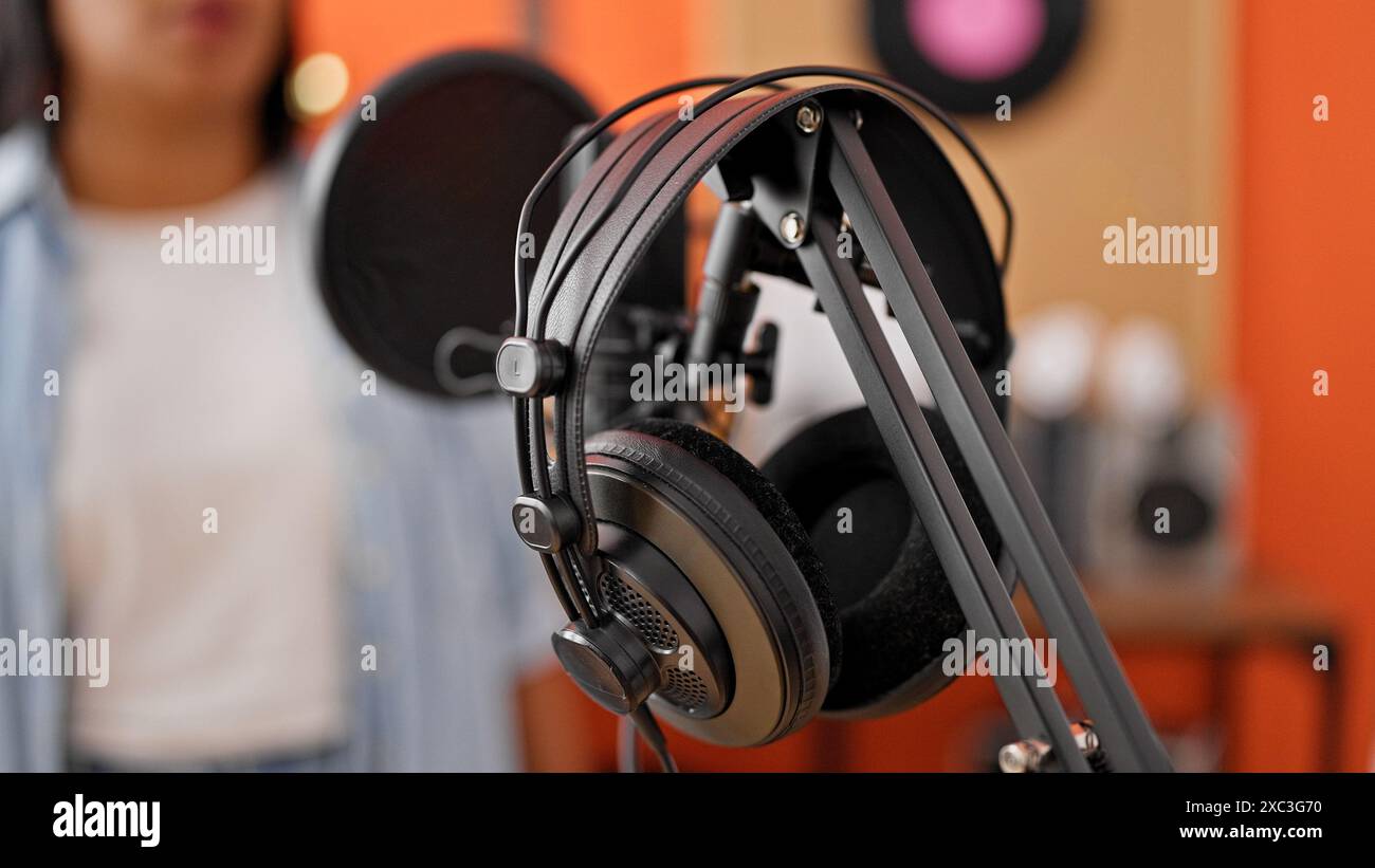 A woman partially blurred in music studio with headphones and microphone capturing audio production ambiance. Stock Photo