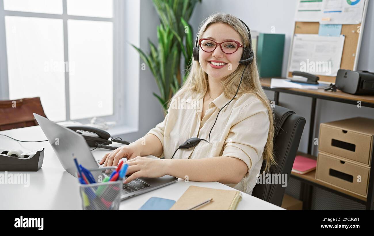 A smiling blonde woman wearing headphones working at her desk in a ...