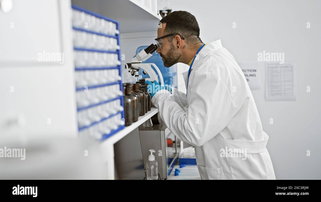 Hispanic man with beard working in laboratory analyzing samples through microscope Stock Photo