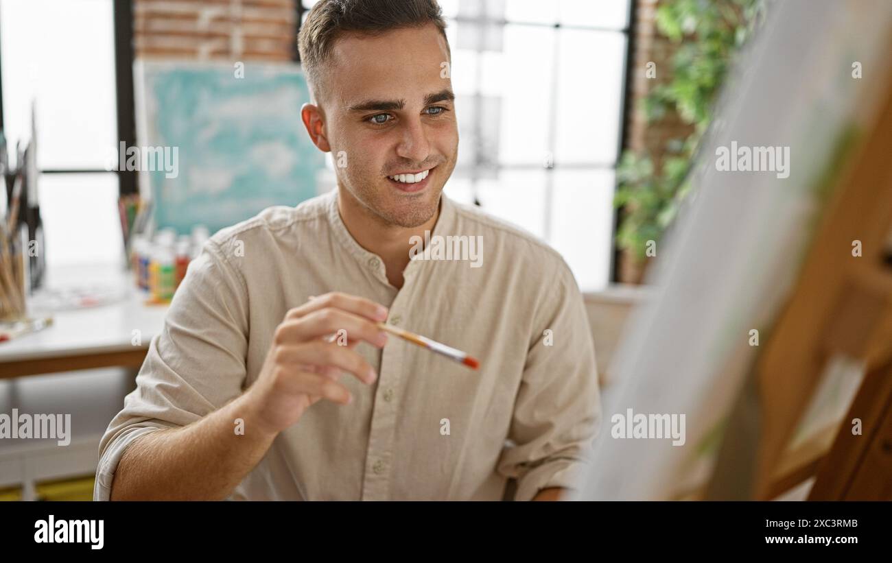 A cheerful young hispanic man painting on an easel in a bright art ...