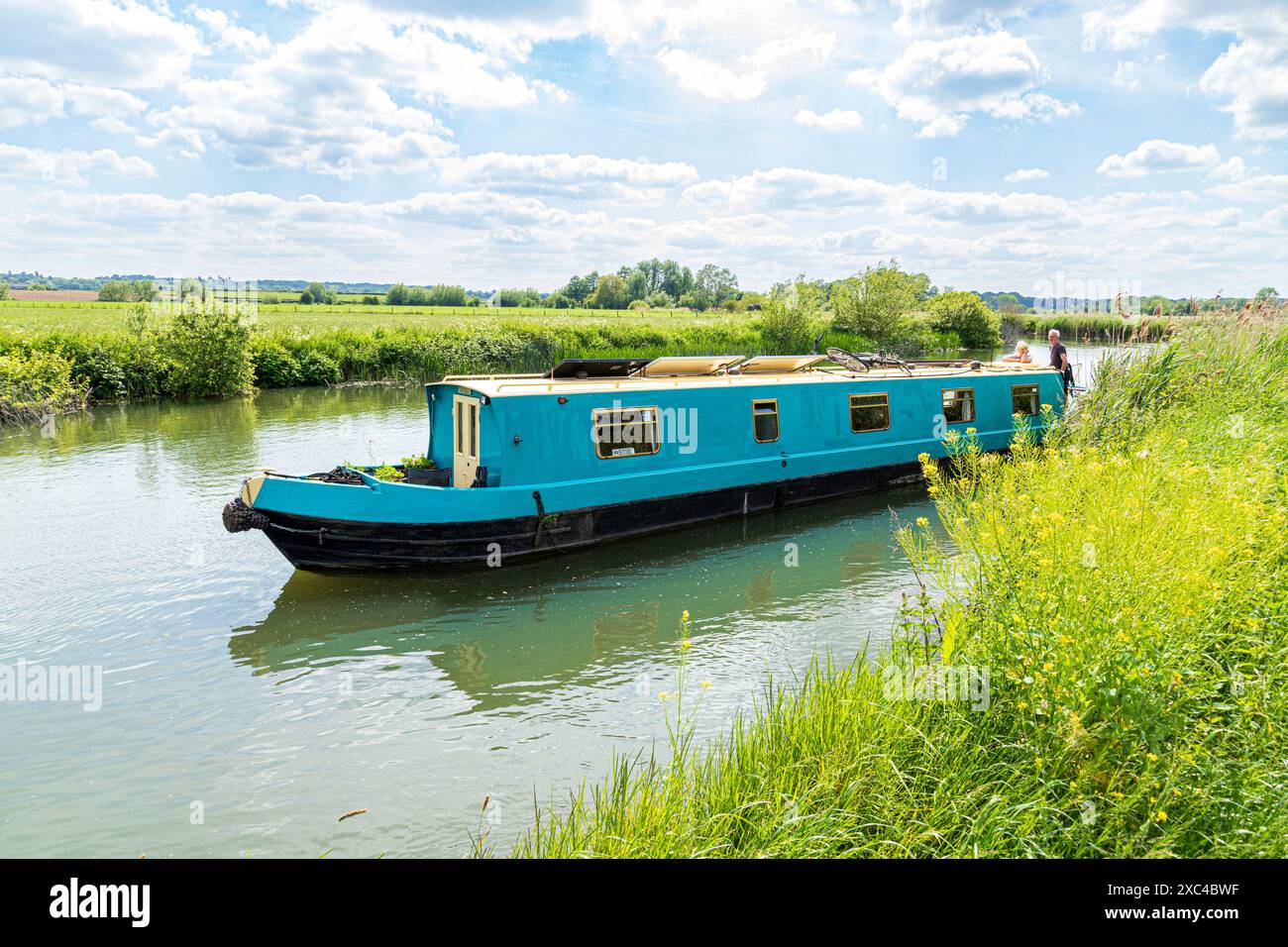 A middle aged couple on a long boat cruising the River Thames at Kelmscott Manor, home of William Morris, Oxfordshire, England UK Stock Photo