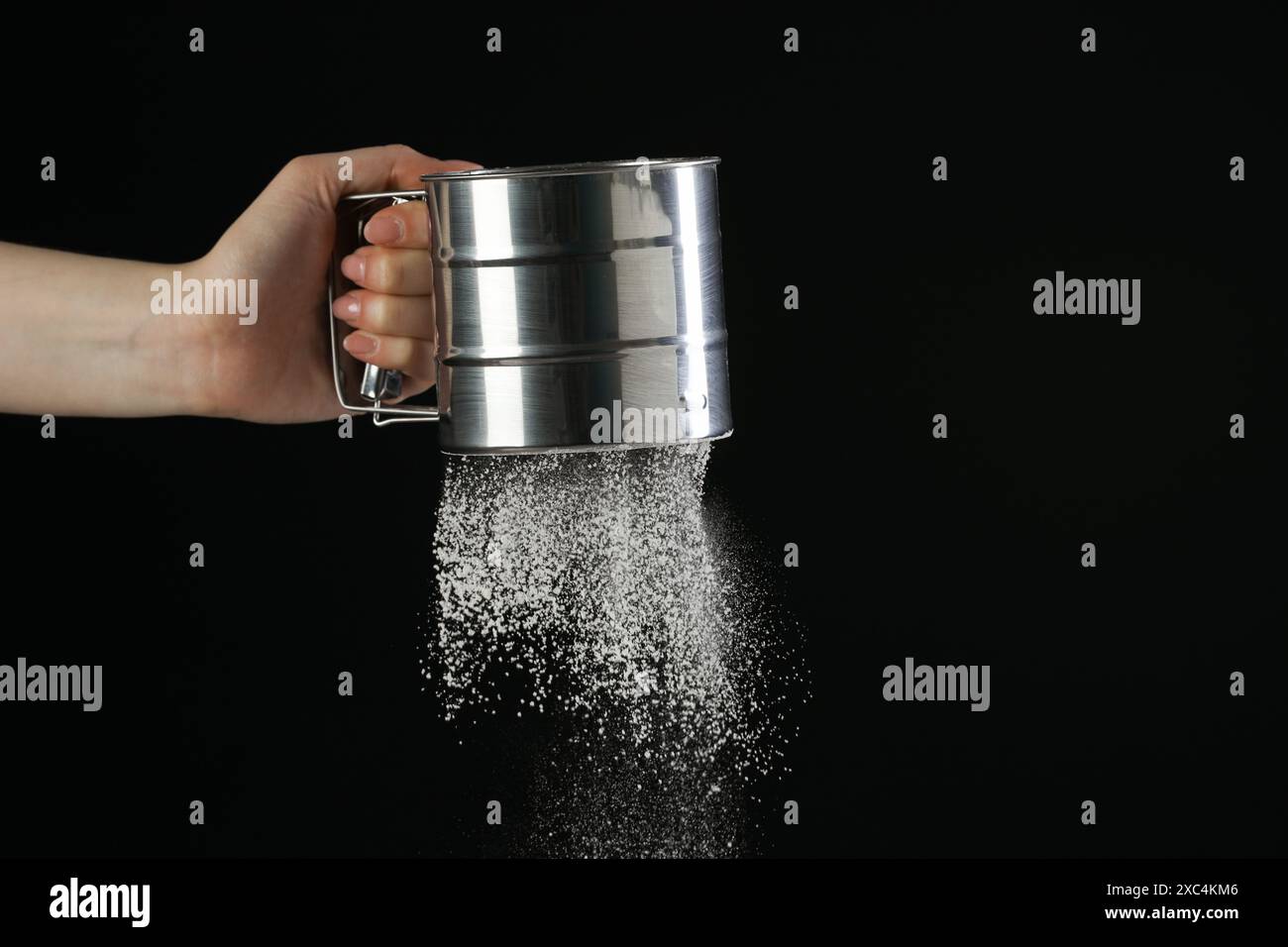 Woman sieving flour against black background, closeup. Space for text ...