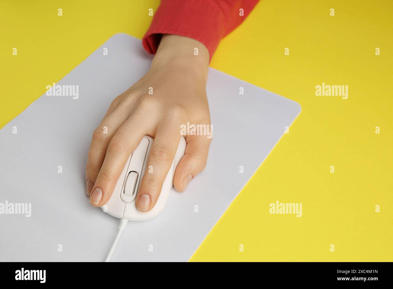 Woman using modern wired computer mouse on yellow background, closeup Stock Photo
