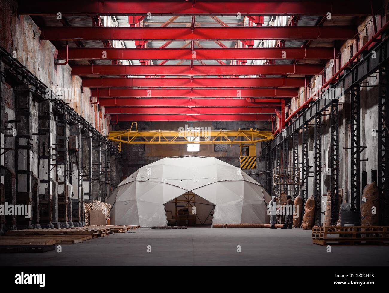 Geometric dome-shaped igloo on the floor of old industrial building. Red transverse beams and yellow overhead crane above. Diminishing perspective. Stock Photo