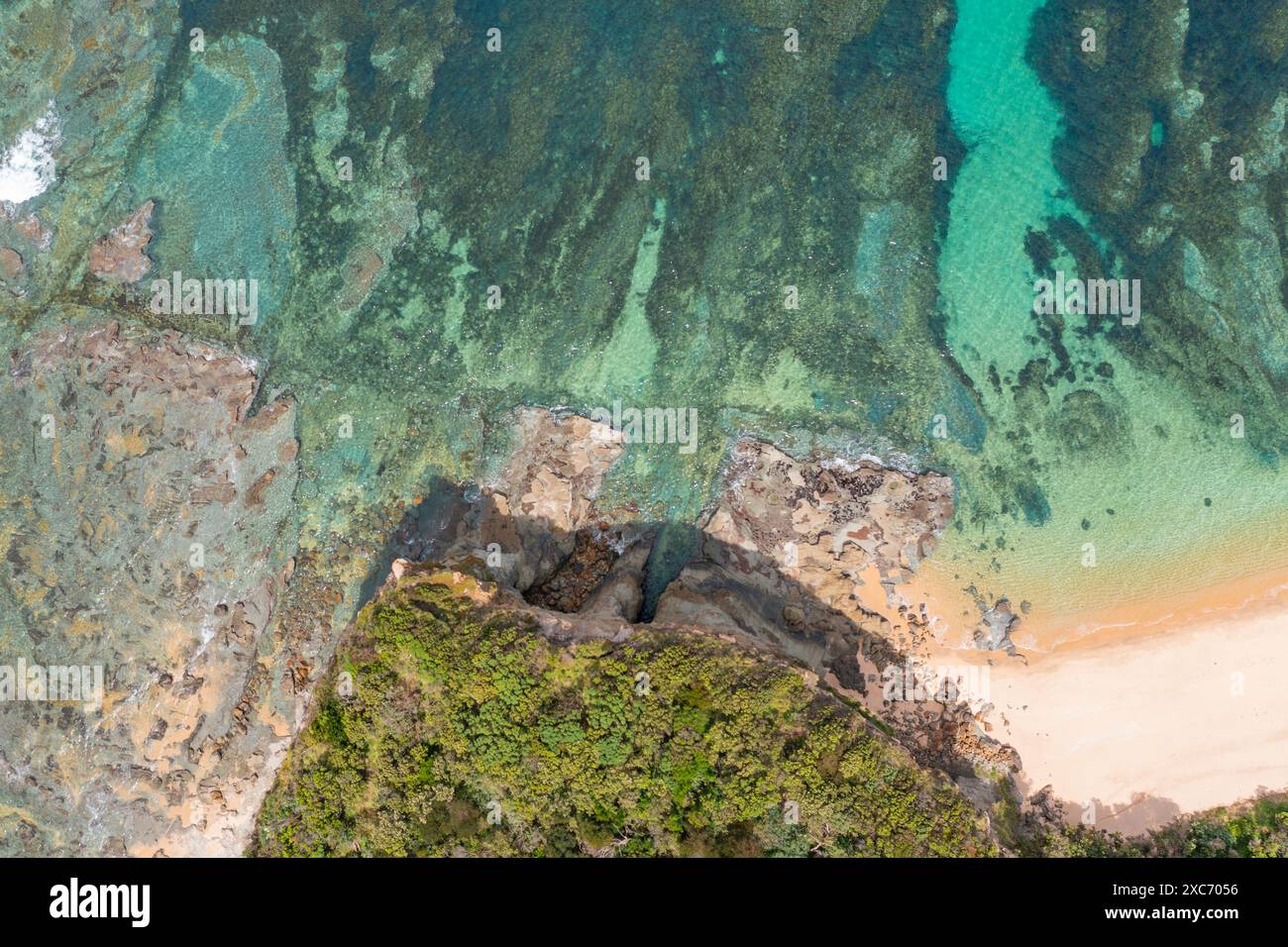 Aerial view looking down on  a rocky reef in front of a coastal headland covered in vegetation at Inverloch in Gippsland, Victoria, Australia. Stock Photo