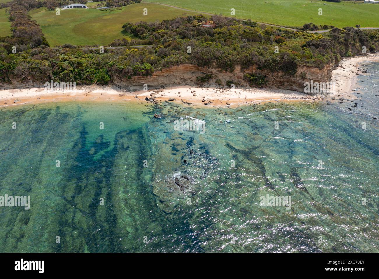 Aerial view of a rocky reef in front of a rugged coastline covered in vegetation at Inverloch in Gippsland, Victoria, Australia. Stock Photo