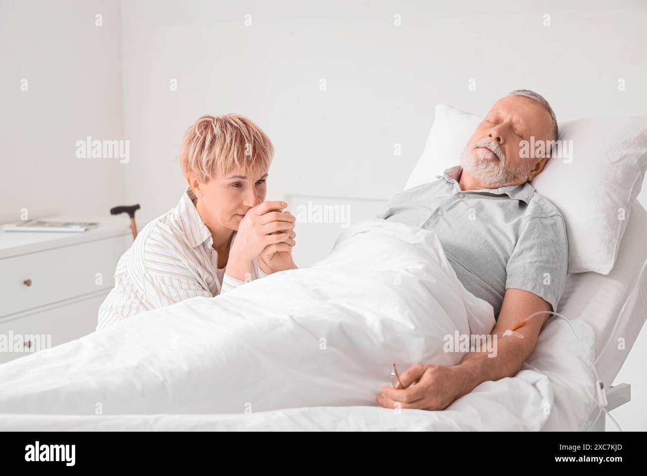 Mature woman holding her sick husband's hand in clinic Stock Photo