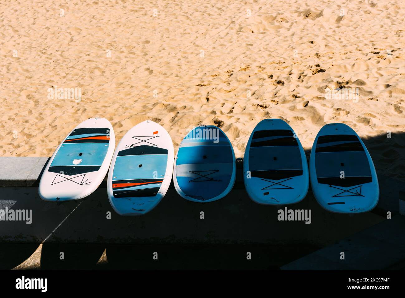 Five stand up paddleboards are lined up on the sand at a beach Stock Photo