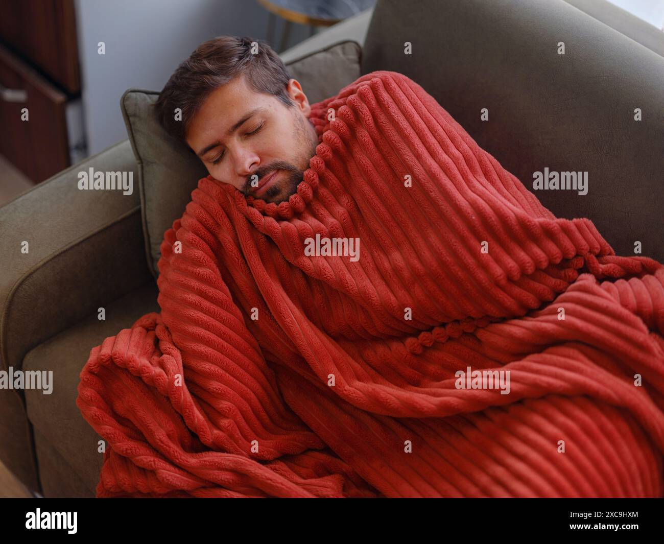 autumn and winter season of sneezes. Young Caucasian Sick man with fever lying on couch . Getting enough restorative sleep helps your body recover and strengthens your immune response. Stock Photo