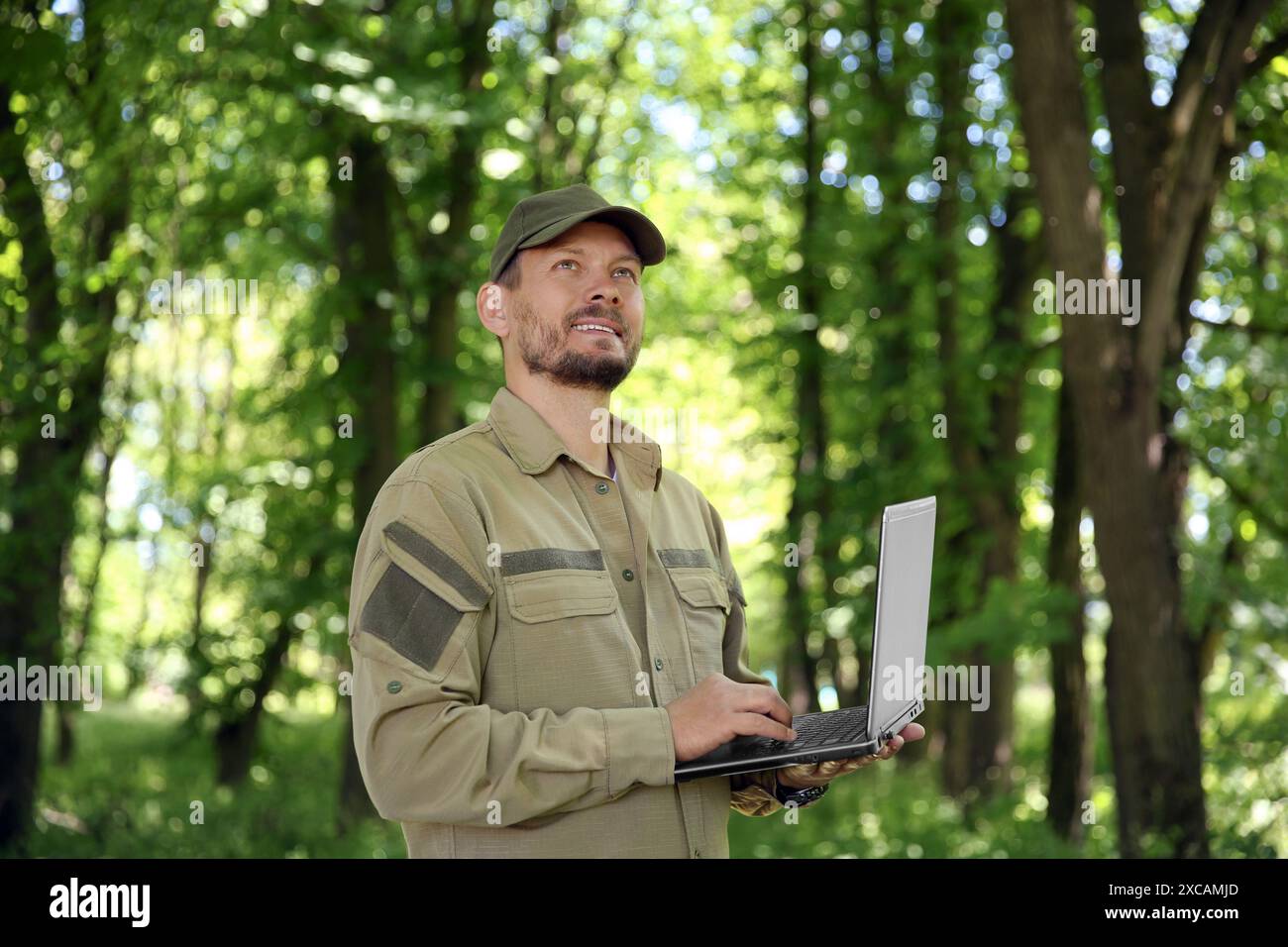Forester with laptop examining plants in forest Stock Photo