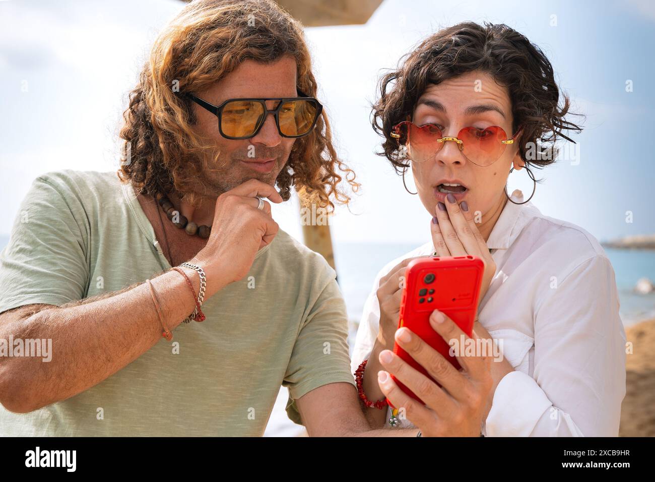 Smiling couple on the beach browsing smartphone apps. Stock Photo