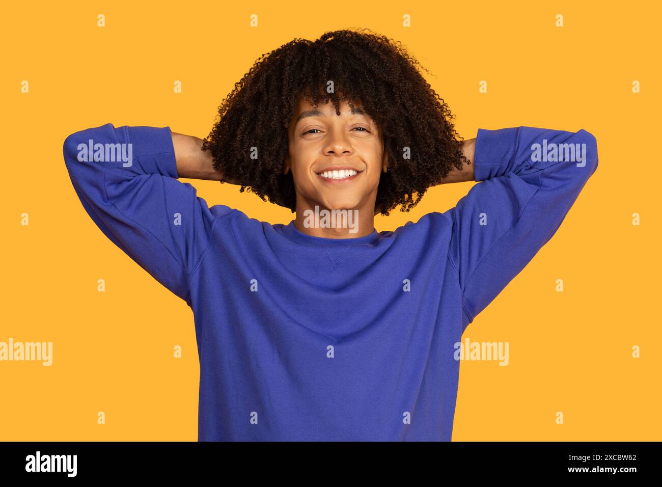 Smiling Young Man With Curly Hair Leaning Back on Yellow Stock Photo
