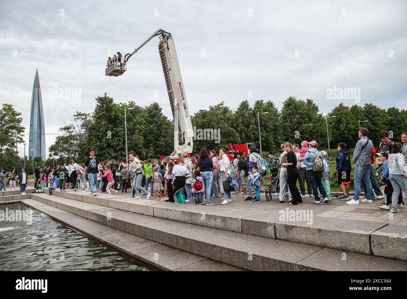 People ride in the cradle of a fire truck during the firemen's festival in the 300th anniversary park against the backdrop of the building of the public and business complex with the headquarters of the Gazprom group Lakhta Center. On June 14, the festival “My Dad is a Fireman, My Dad is a Hero” was held in the park for the 300th anniversary of St. Petersburg. Visitors were treated to interactive platforms, spectacular demonstrations by rescuers extinguishing a burning car, as well as a concert program and a field kitchen. (Photo by Artem Priakhin/SOPA Images/Sipa USA) Stock Photo