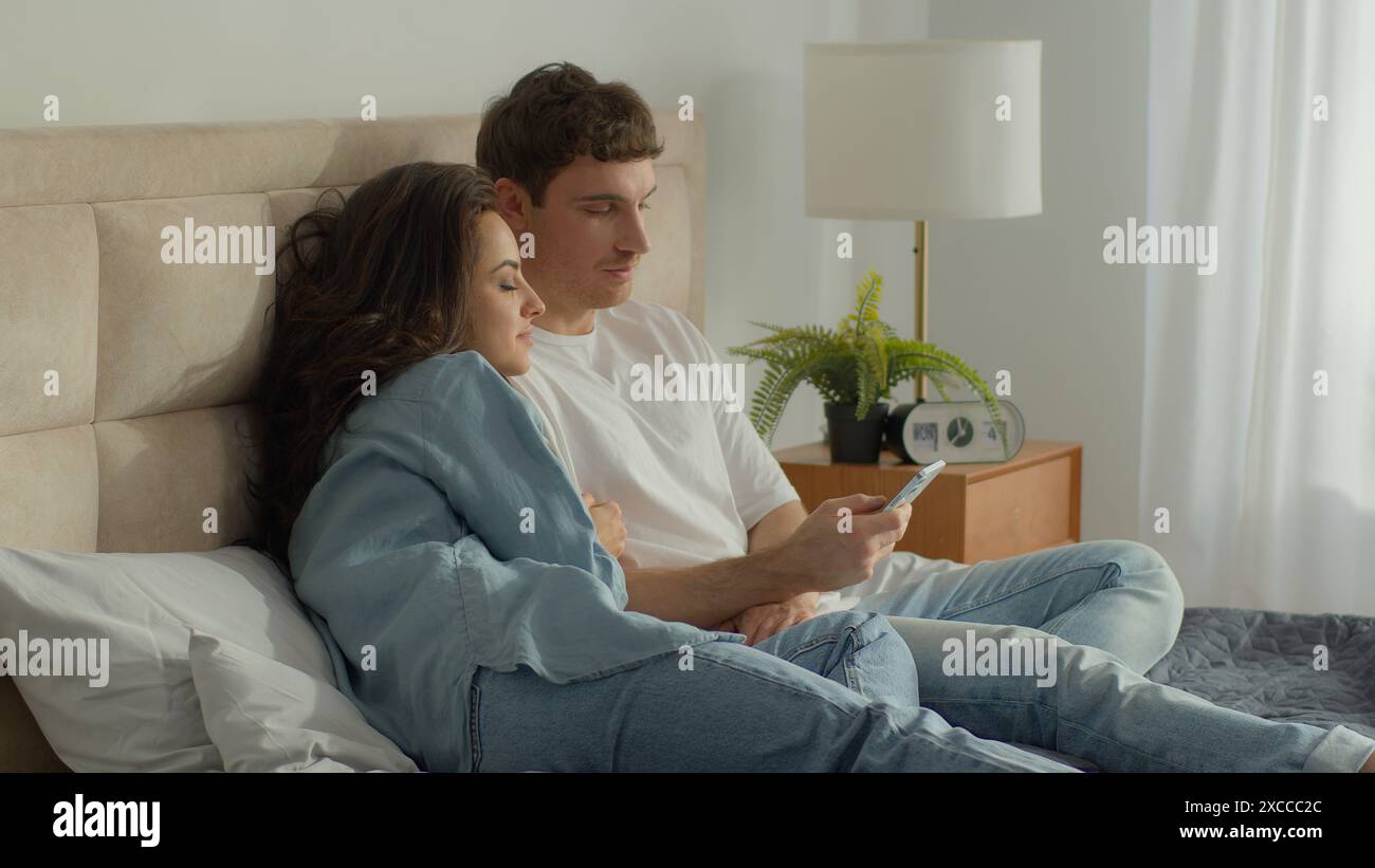 Couple lying bed resting bedroom man woman talk mobile phone smartphone ...