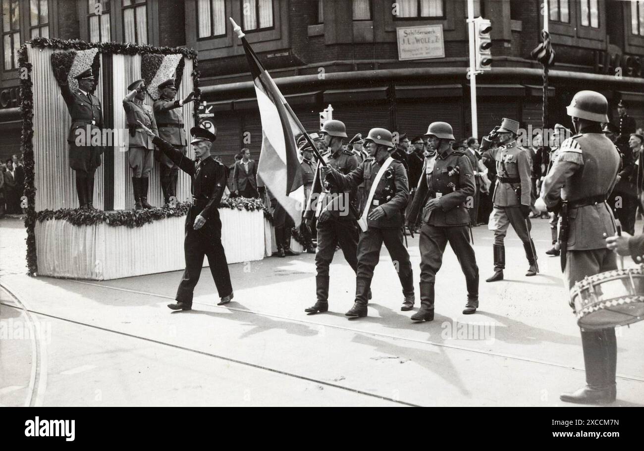 A parade of the Dutch Volunteer Legion of the Waffen SS on Grote Marktstrasse in The Hague in 1941. On the platform are General Friedrich Christiansen (left), Lt-General Hendrik Seyffardt (middle) and SS-Obergruppenfuehrer Hanns Albin Rauter (right). Seyffaardt is wearing his Dutch army uniform (which was an act of treason). He was assassinated by Dutch resistance in 1943. Stock Photo