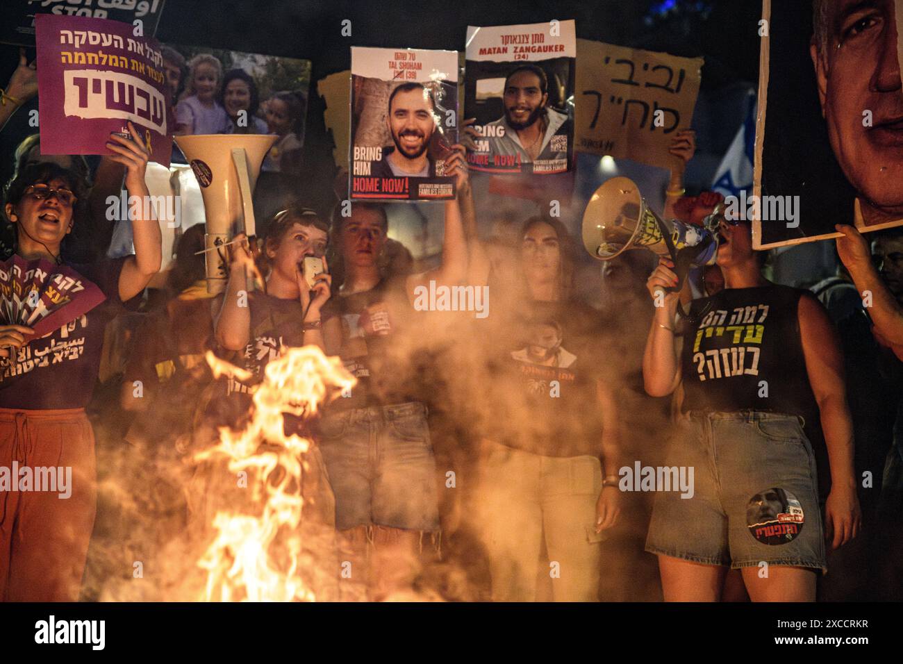 Israel. 15th June, 2024. Ella Havron, family member of Israeli hostage Tal Shoham, and Natali Zangauker, sister of Israeli hostage Matan Zangauker hold up signs with their photos in front of a bonfire. Over 100,000 of Israelis demonstrated with the hostages families against Prime Minister Benjamin Netanyahu, demanding an immediate hostage deal and ceasefire as they set up bonfires on Kaplan Junction. Tel Aviv, Israel. June 15th 2024. (Matan Golan/Sipa USA). Credit: Sipa USA/Alamy Live News Stock Photo