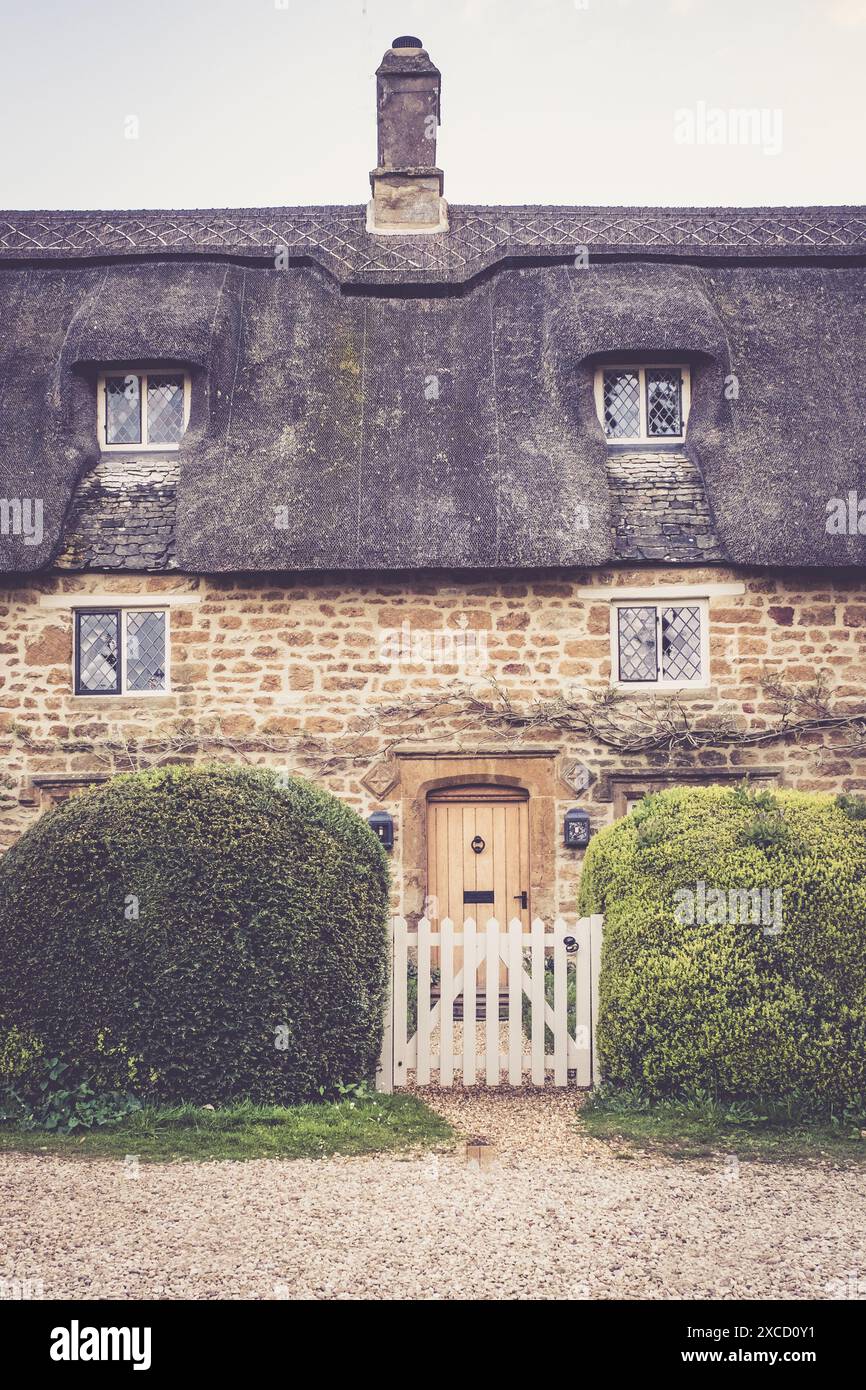 A charming stone cottage with a thatched roof and a white picket fence ...