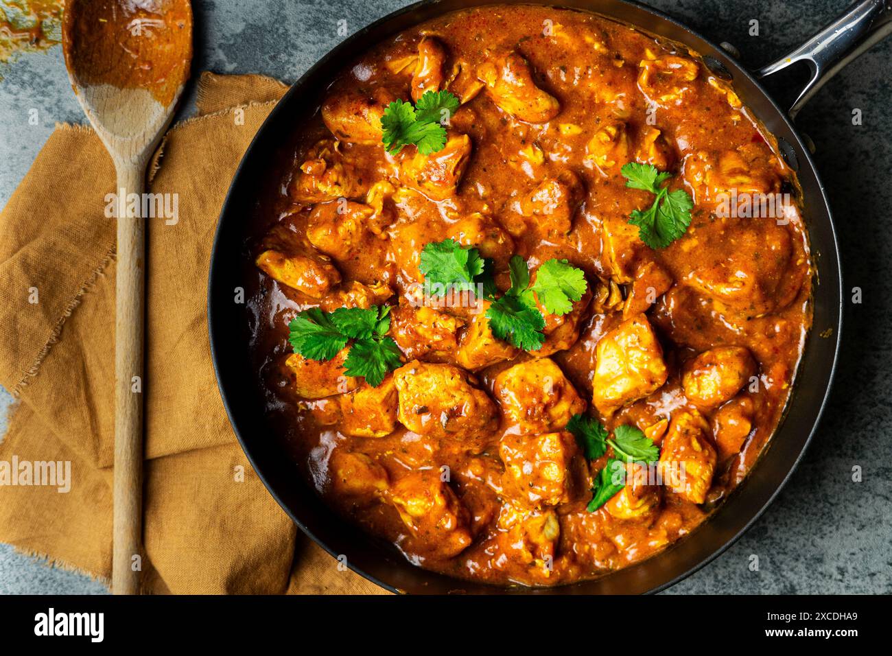 Overhead shot of chicken curry in a pan with a wooden spoon with napkin on kitchen counter Stock Photo