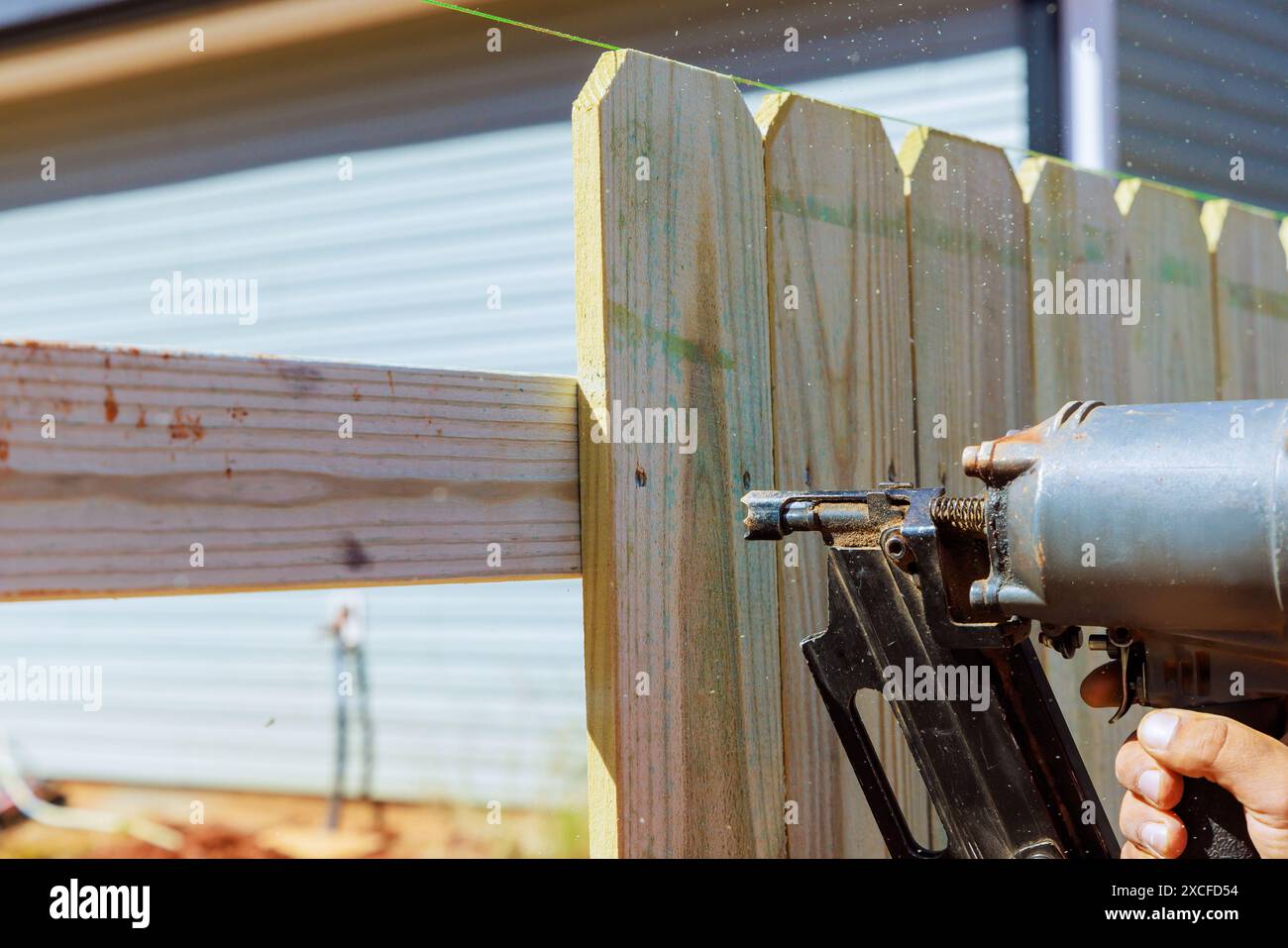Nailer using air pneumatic gun to secure wooden plank fence during work
