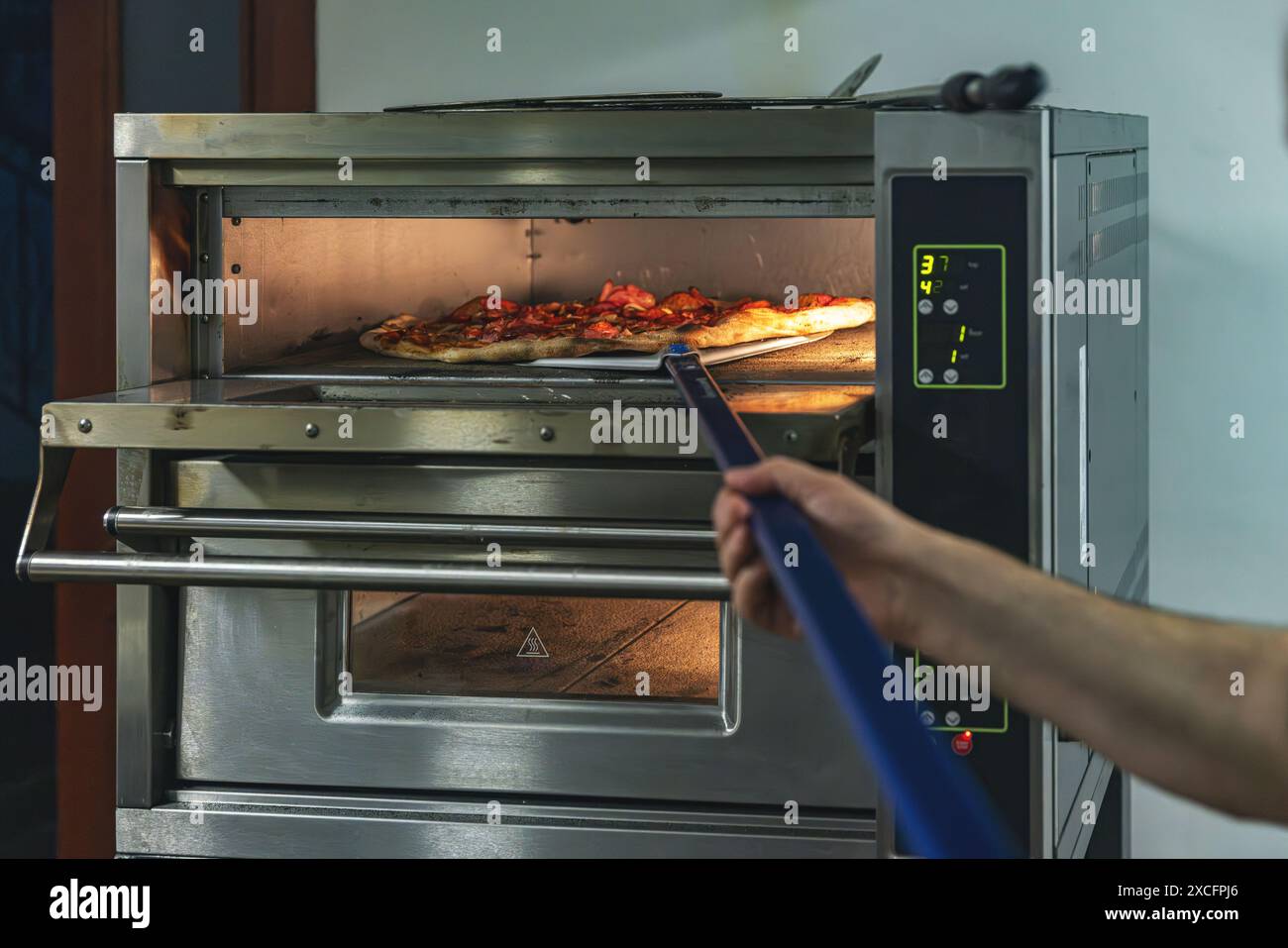 Chef monitors a pizza cooking in a professional oven with digital controls Stock Photo