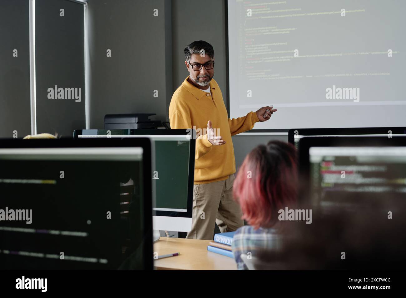 Modern mature teacher of Computer Science standing in front of students ...