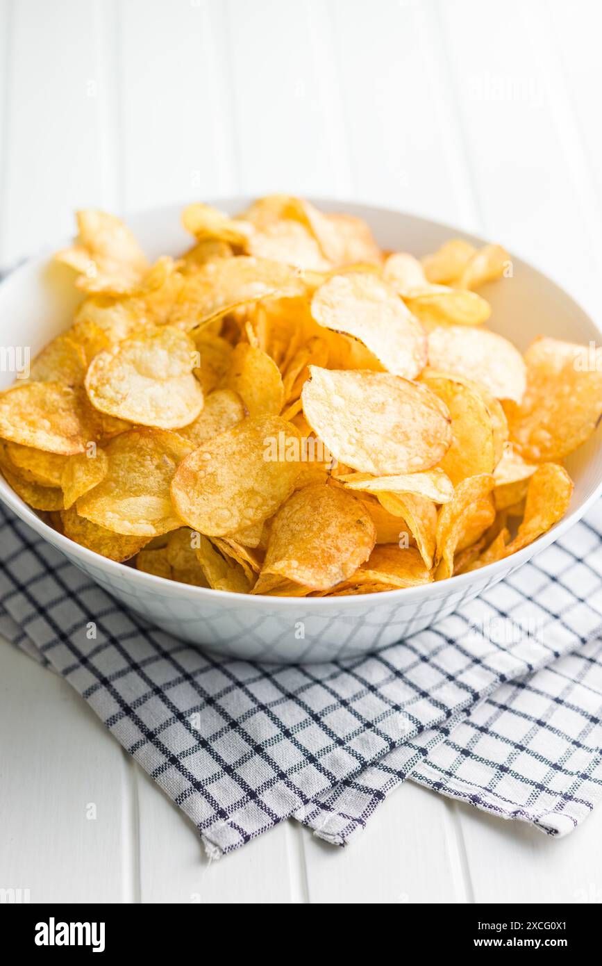 Crispy Potato Chips in bowl on a white table. Stock Photo
