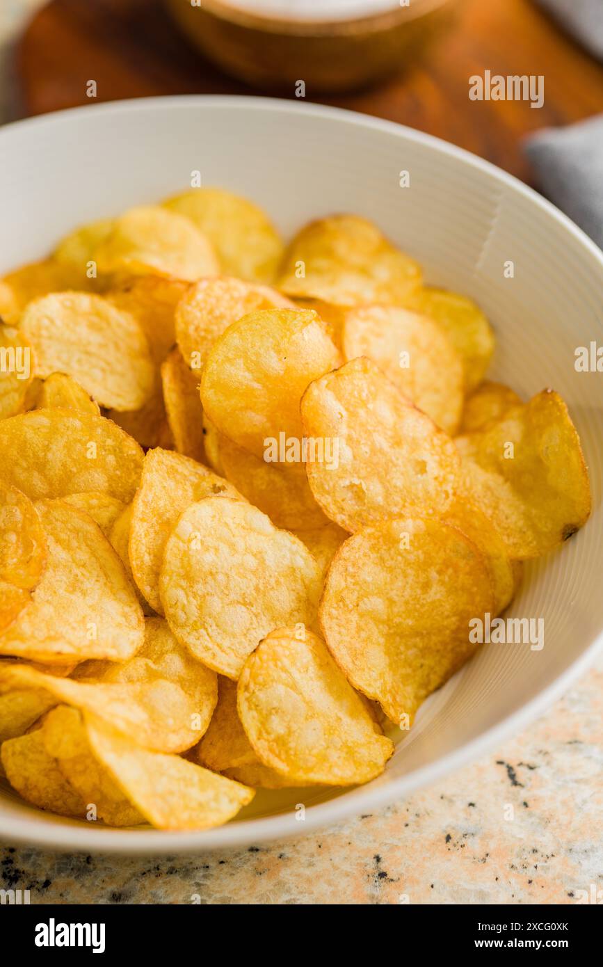 Crispy Potato Chips in bowl on a kitchen table. Stock Photo