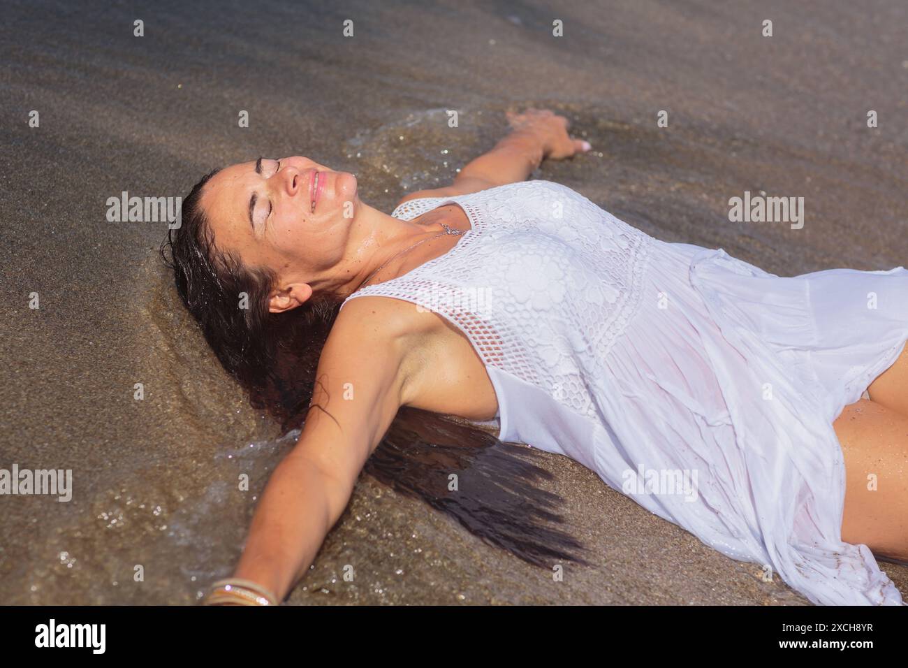 Happy mature woman in wet white dress lying on sandy shore Stock Photo -  Alamy
