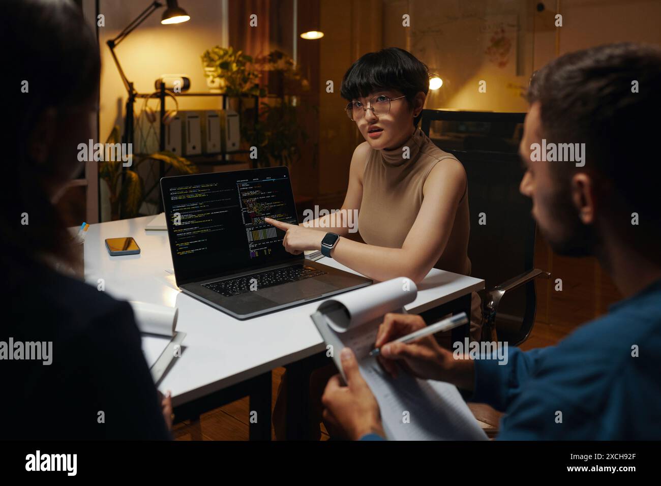 Developer showing programming code on laptop screen and discussing with team Stock Photo