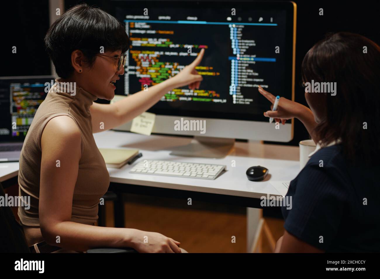 Female developers discussing programming code on computer screen Stock Photo
