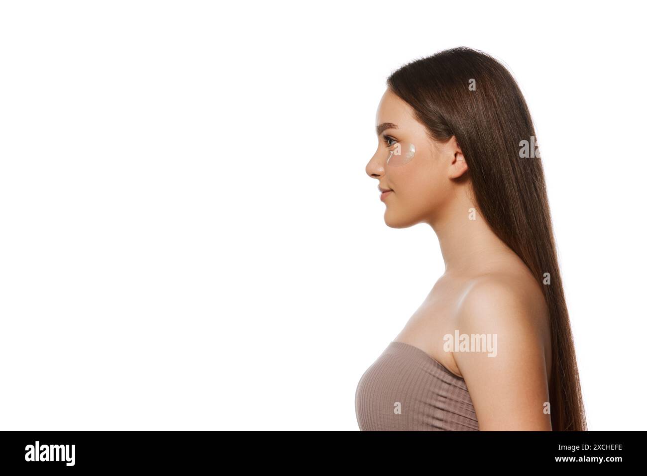 Side view portrait of young woman with long brown straight hair and perfect well-kept skin standing isolated on white background Stock Photo