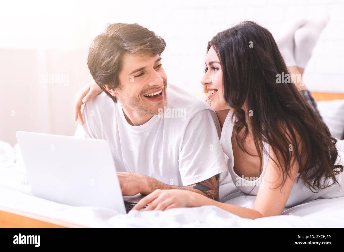 Happy Couple Laughing While Using Laptop in Bed Stock Photo